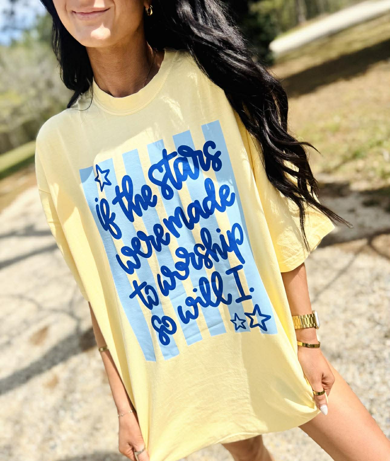 Person wearing a yellow t-shirt with blue text and star graphics outdoors.
